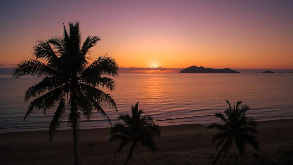 The Sun Is Setting Over The Ocean With Palm Trees In The Foreground — Mission Solar And Electrical In Mission Beach, QLD