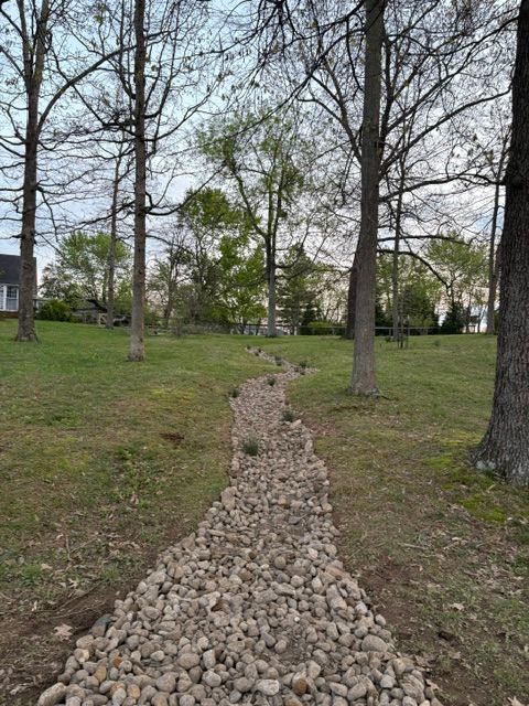 A gravel path going through a grassy field surrounded by trees