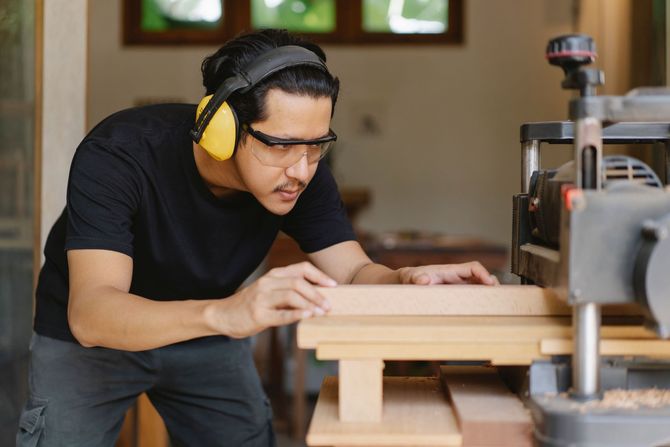 Man wearing hearing protection inspects wood on a table saw in a workshop