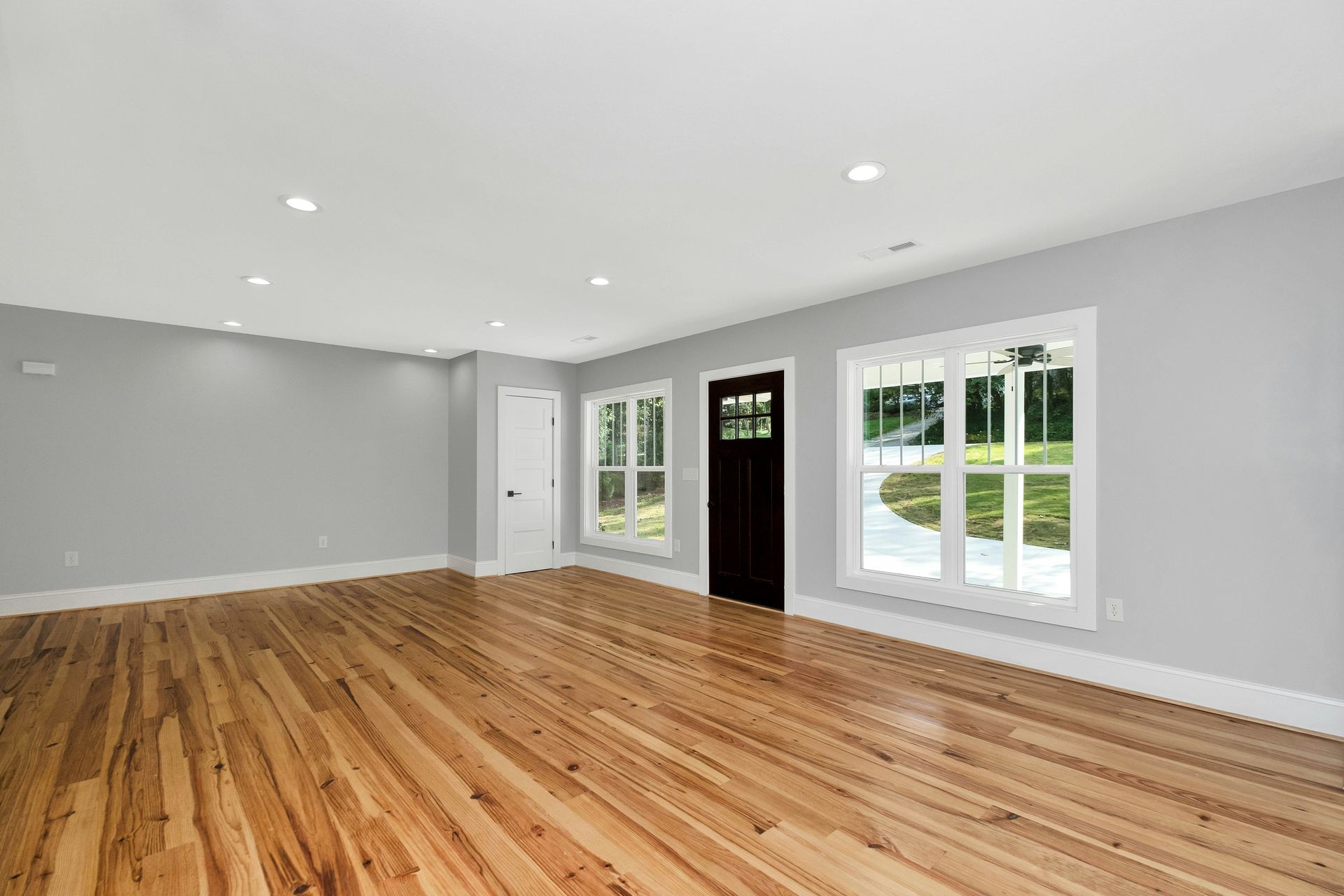 Empty living room with hardwood floors, gray walls, white trim, and French doors to a bright yard