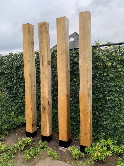 Een rij houten palen die naast elkaar voor een heg staan.