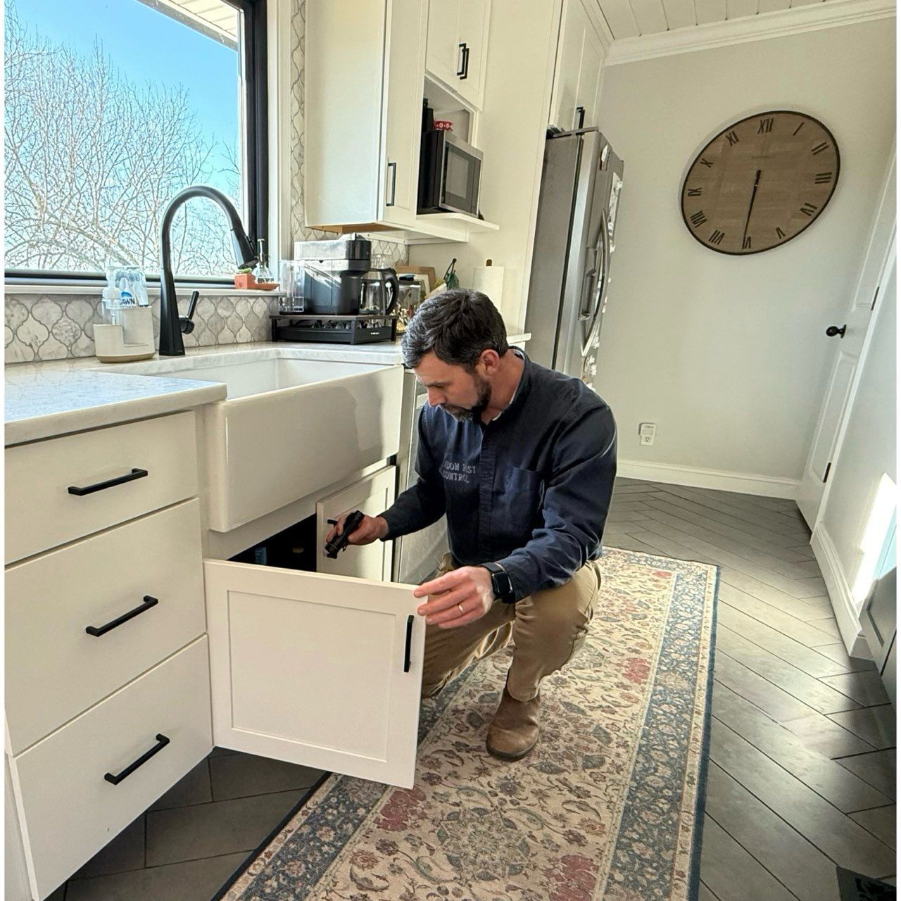 A man is kneeling down in a kitchen looking into a cabinet.