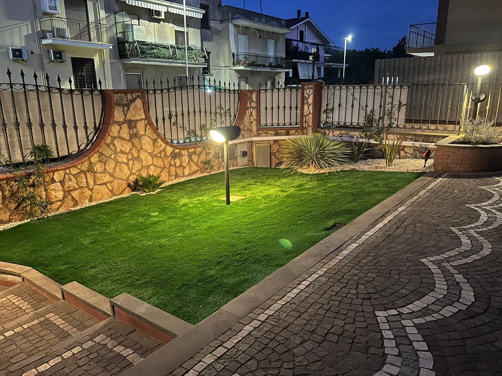 Un piccolo cortile anteriore ben illuminato con erba verde, muri in pietra e un sentiero decorato al tramonto.