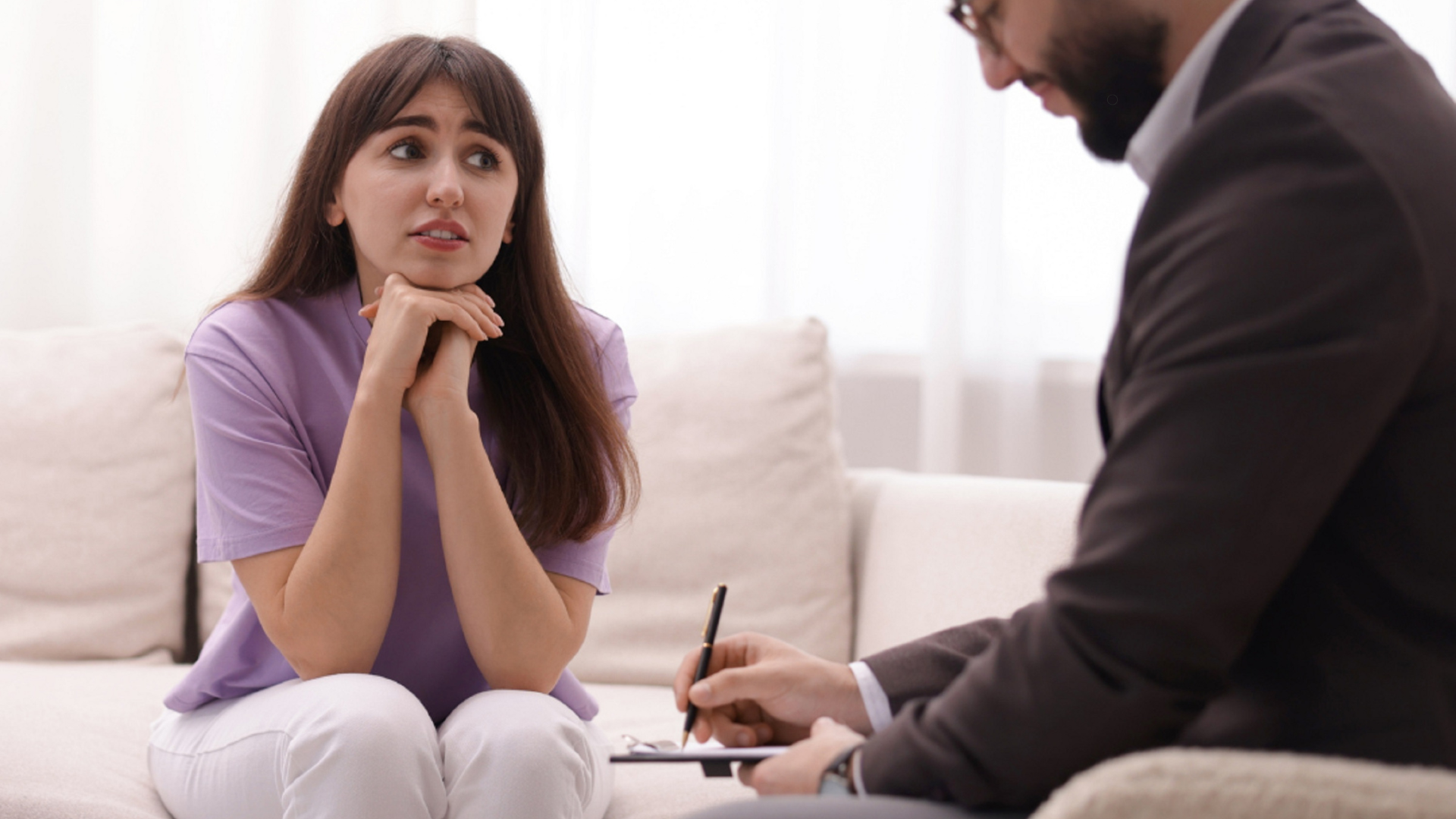A woman in a purple shirt looks concerned while speaking with a mental health professional, showing a moment of therapy or counseling