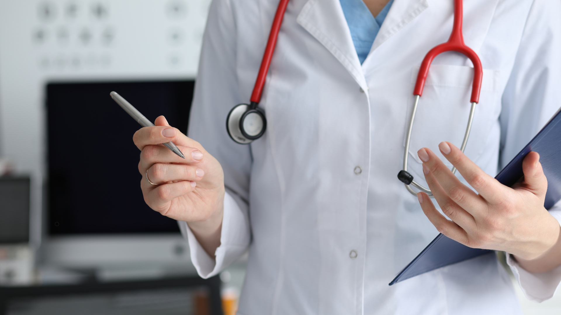 A healthcare professional wearing a white coat is holding a pen and a clipboard while explaining something to a patient. The background shows an eye chart and a computer, indicating a medical setting.