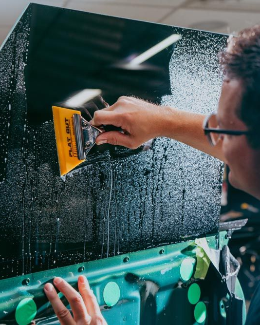 Person applying tint to a car window with a squeegee.