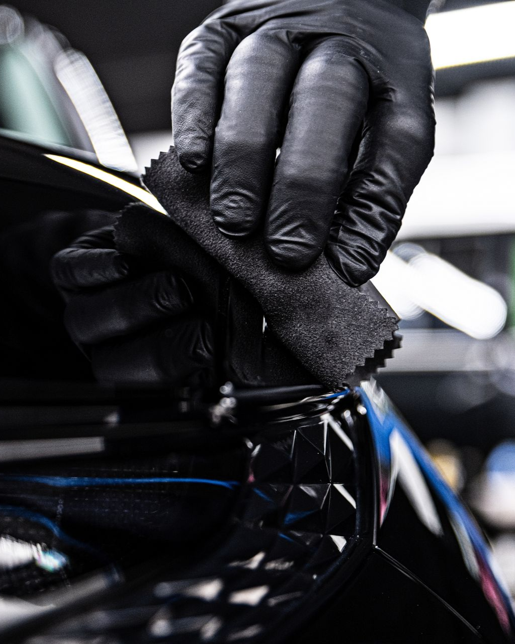 Black-gloved hands applying a black coating to a car's black surface with an applicator.
