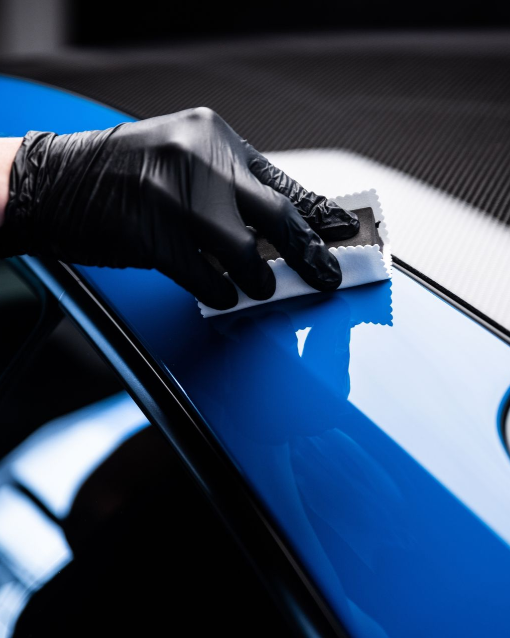 Gloved hand applying ceramic coating to a shiny blue car surface.