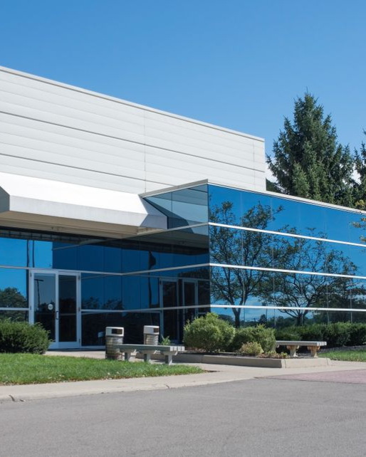 Modern office building with reflective blue windows and white exterior under a clear sky.