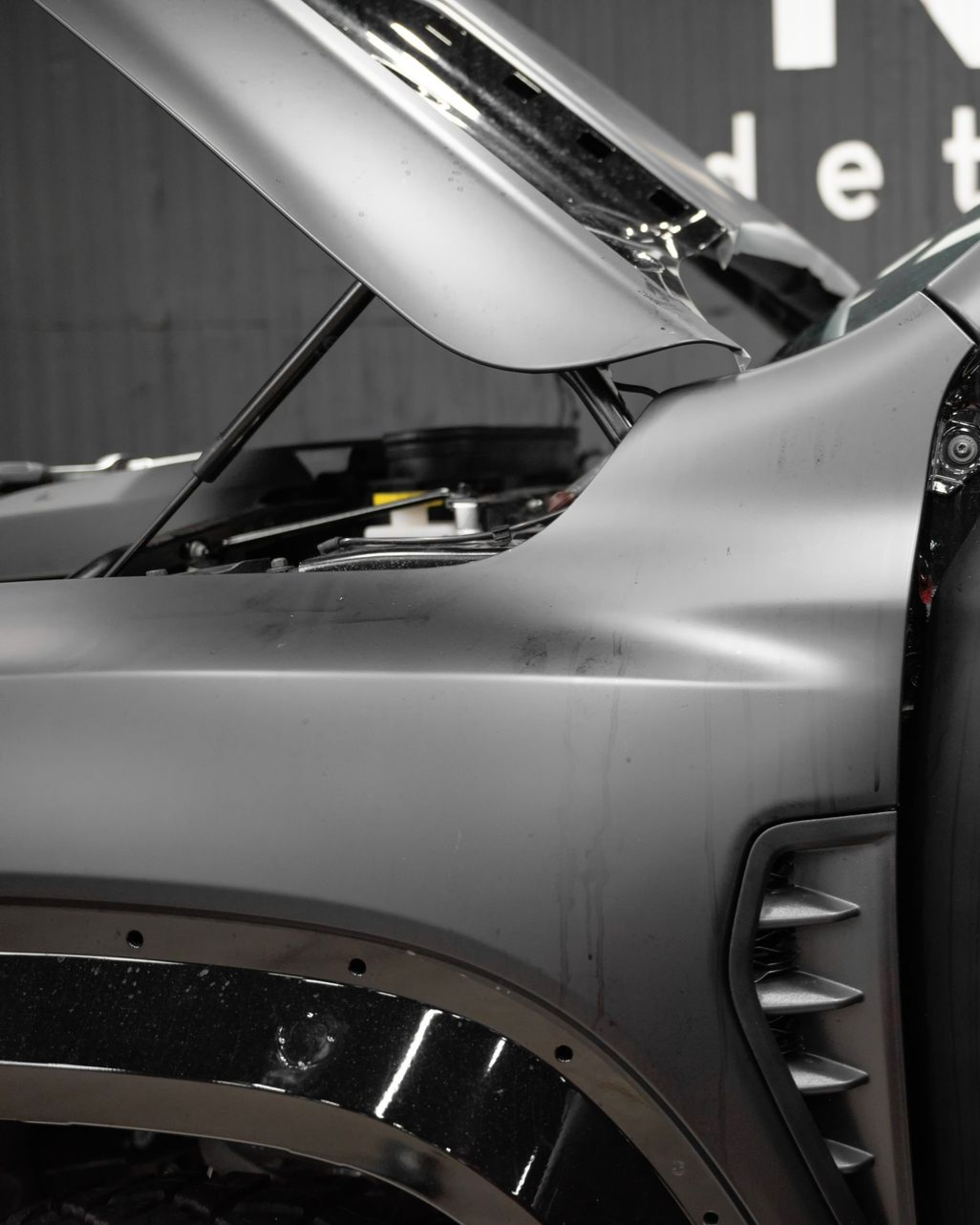 Gray car with open hood, showing details of the front panel, vents, and wheel arch.