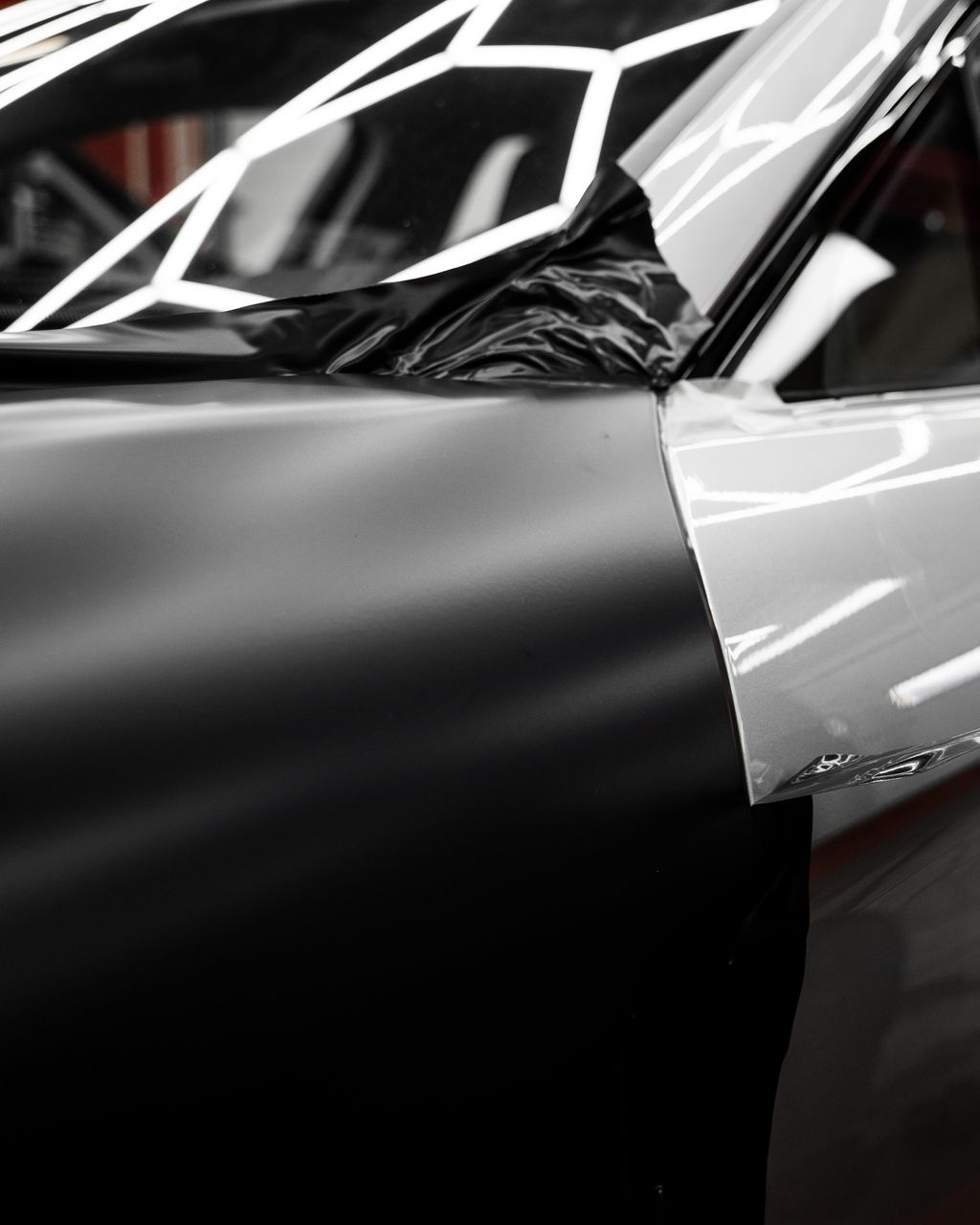 Car door being wrapped in black vinyl, partially finished with white.