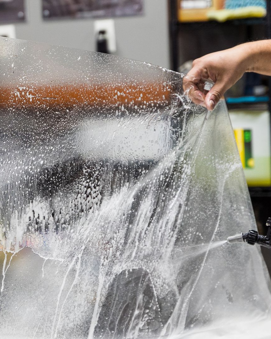 A person is applying a clear film to the hood of a car.