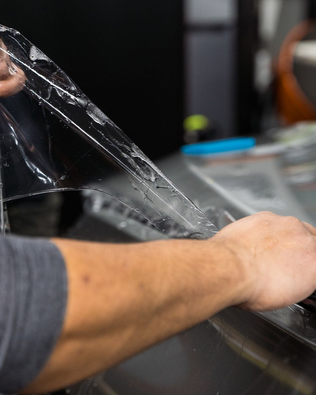 Person peeling protective film from a surface in a workshop setting.