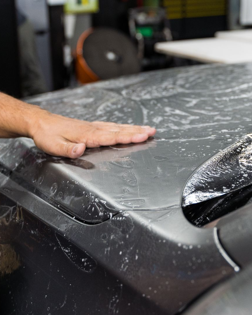 A car is covered in plastic wrap in a garage.