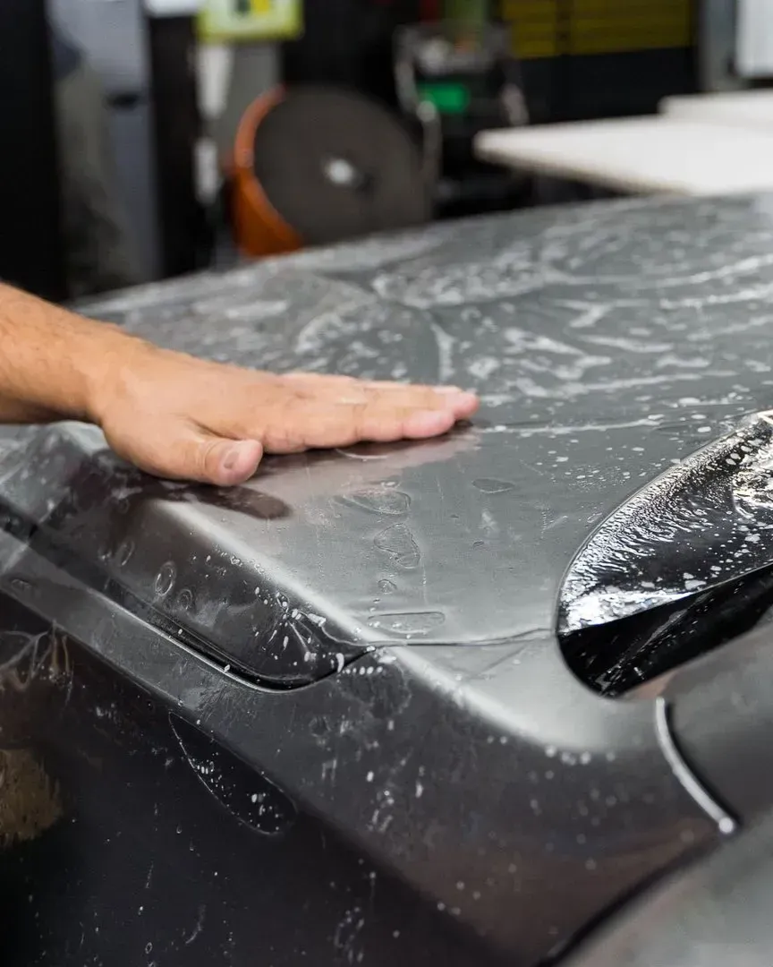 Technician smoothing paint protection film onto a car hood during installation