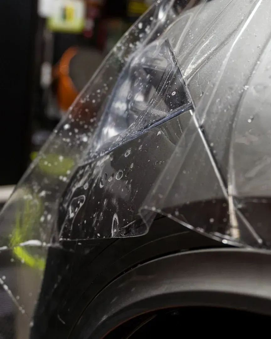 Paint protection film being applied over a black car's headlight and bumper