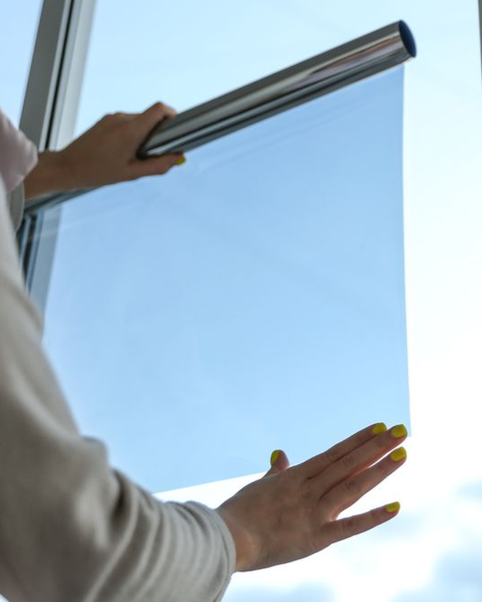 Person holding blue window film near a window; the sky is visible through the film.