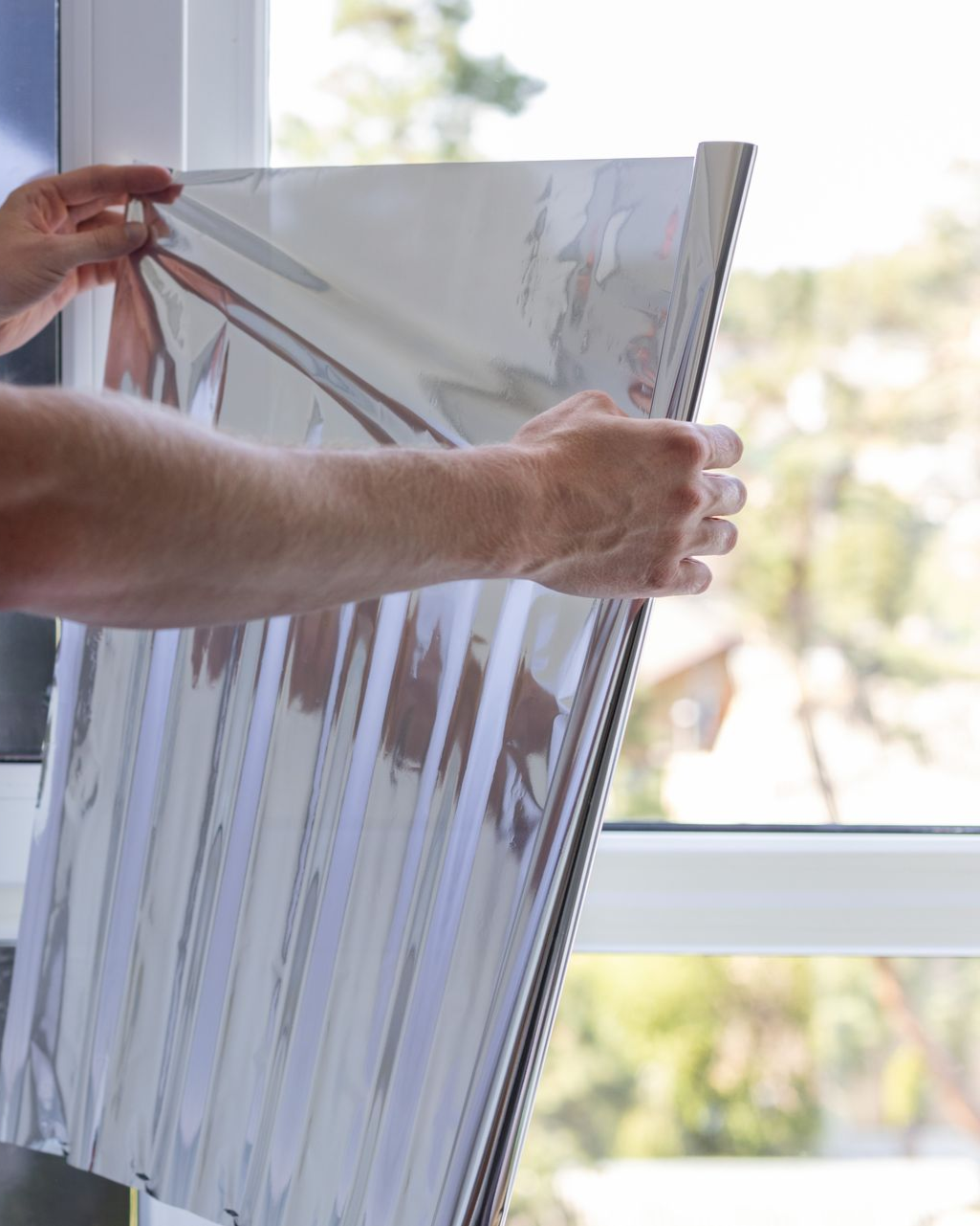 Hands holding a reflective foil sunshade up to a window.