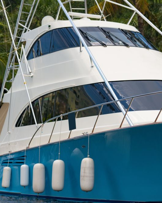 Blue and white yacht on water, with white fenders hanging from the hull and a white frame extending above the top deck.