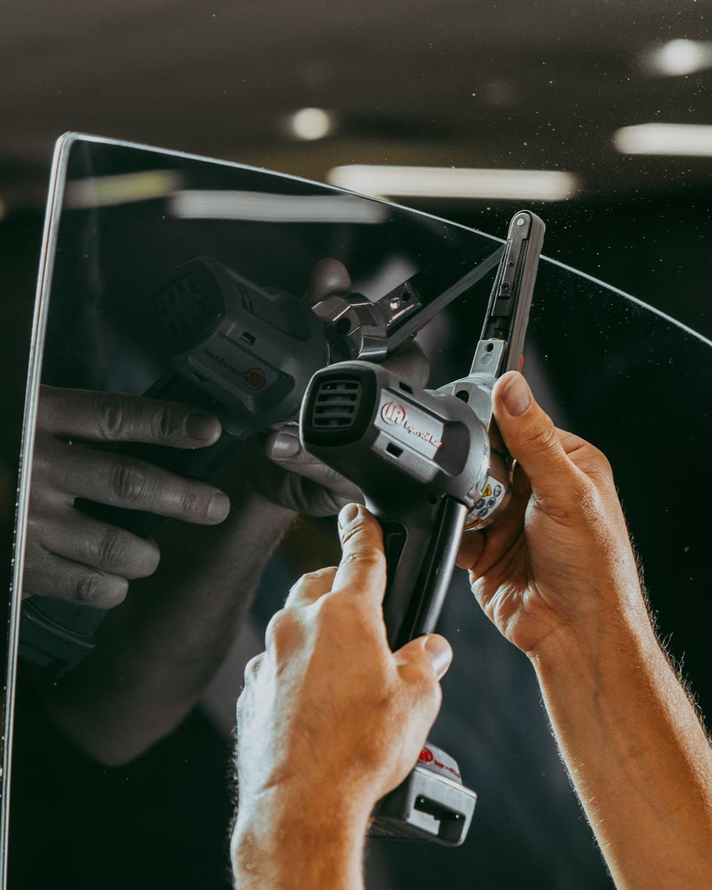 Person using a heat gun on tinted glass, hands visible.