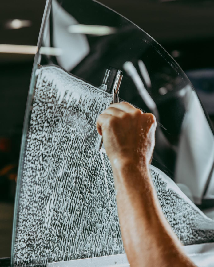 Hand using a tool to apply tint to a car window.