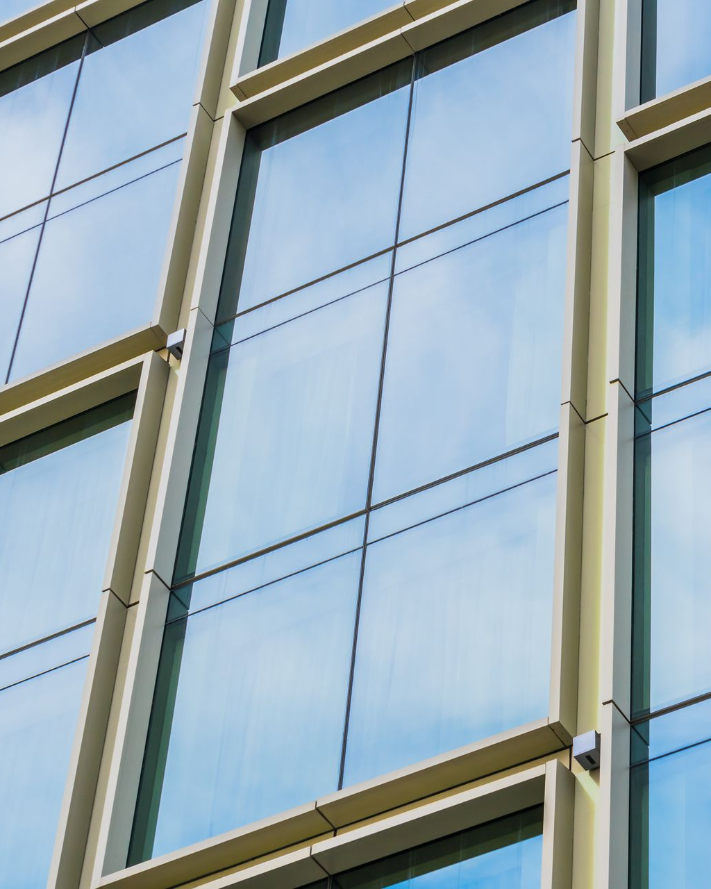 Close-up of a modern building facade with large glass windows reflecting the sky and supported by beige frames.