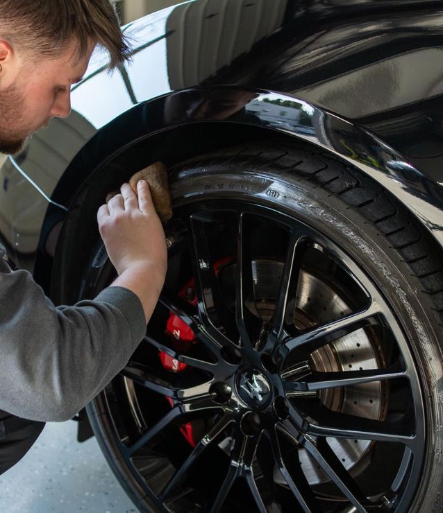 A man is cleaning the wheel of a black car with a sponge.