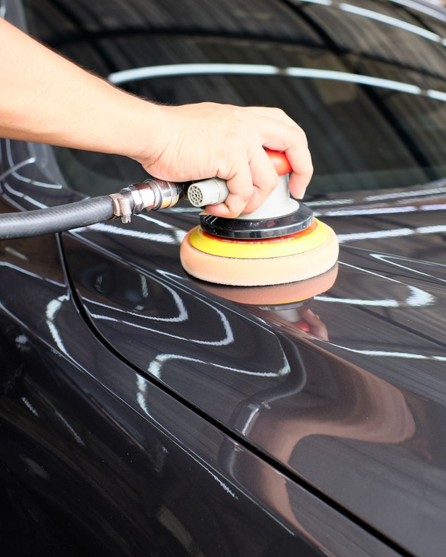Hand polishing a dark car with an electric polisher.