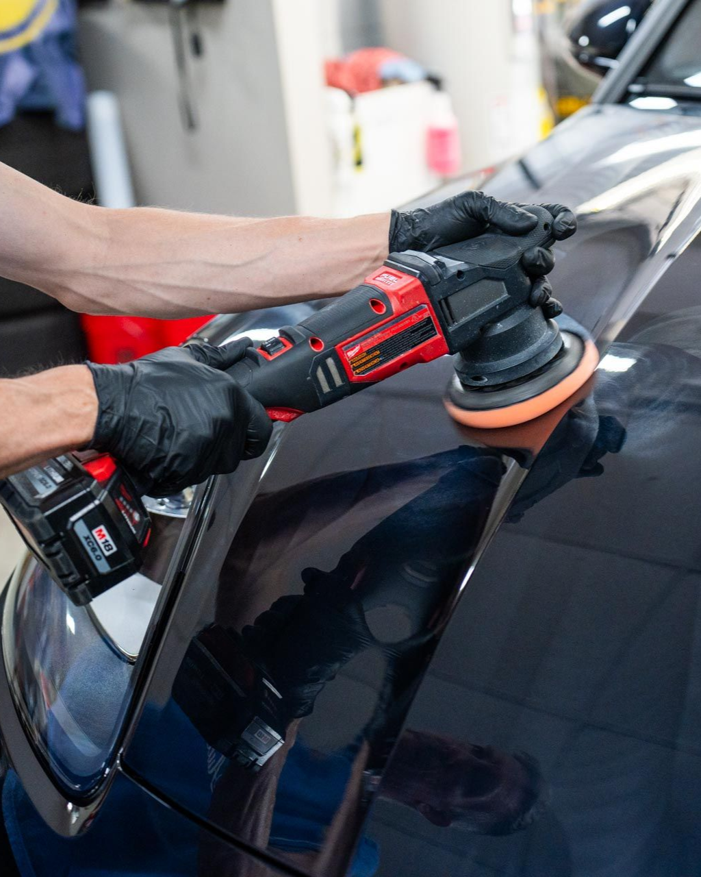 A person wearing black gloves is polishing a black car