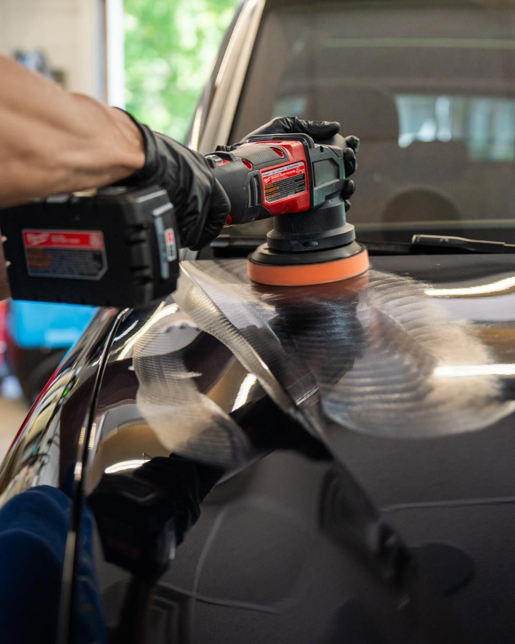 Black-gloved hand using a power buffer on a black car hood.
