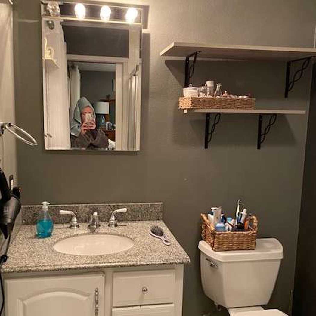 A bathroom with a sink , toilet , mirror and shelves.