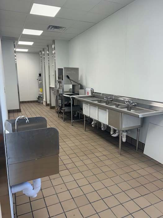 A kitchen with stainless steel sinks and a tiled floor.