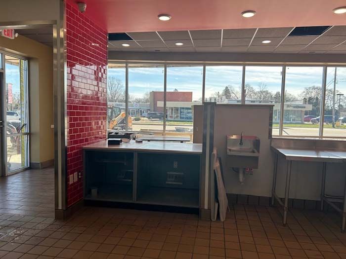 An empty restaurant with a red brick wall and a lot of windows.