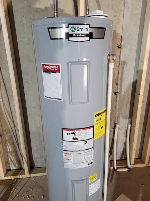 A gray water heater is sitting in a basement next to a wall.