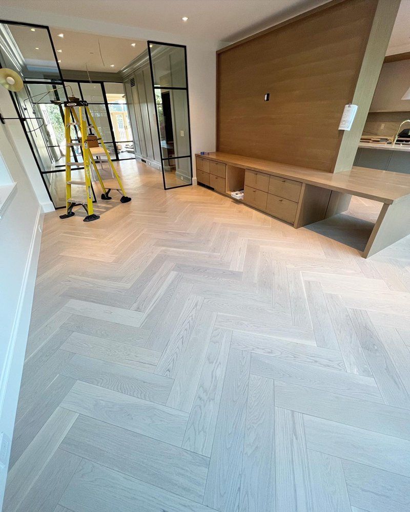 A living room with a herringbone wooden floor and a ladder.
