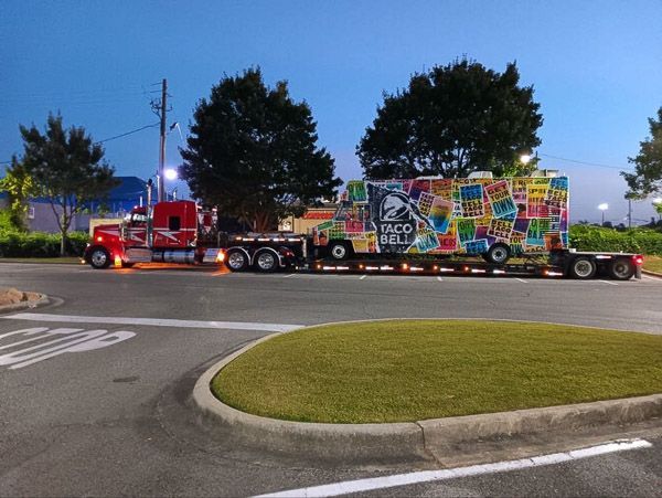 A taco bell truck is being towed by a semi truck