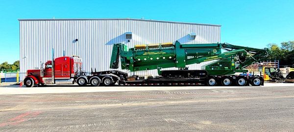A semi truck is carrying a large green machine on a trailer.