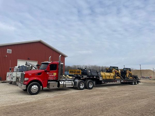 A red semi truck is parked in front of a red barn.