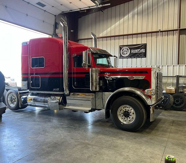 A red and black semi truck is parked in a garage