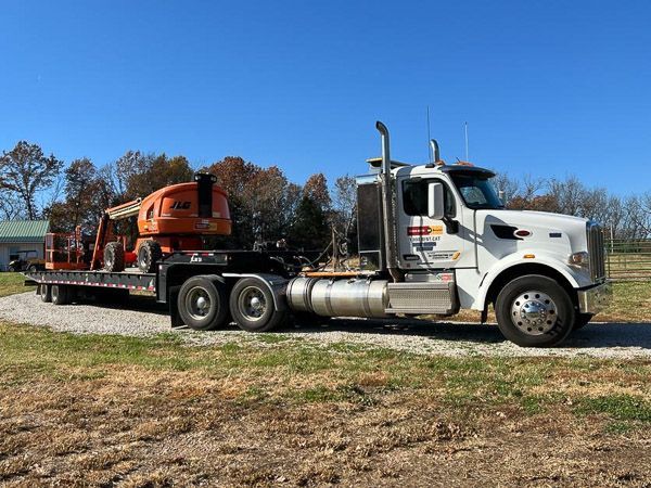 A semi truck with a flatbed trailer is parked in a field.