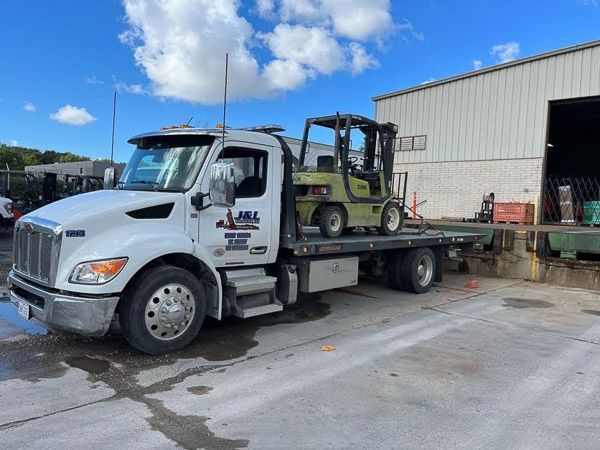 A tow truck is carrying a green forklift on the back of it.