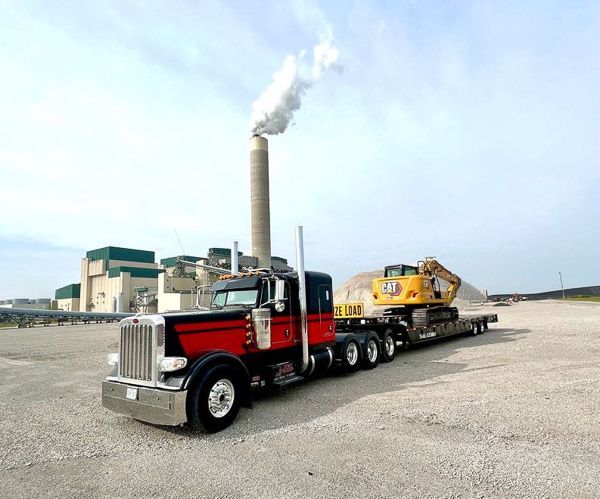 A red semi truck is carrying a yellow excavator on a trailer.
