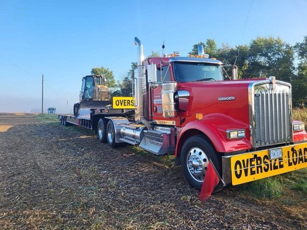A red semi truck with a yellow sign on the front that says ' oversize load '