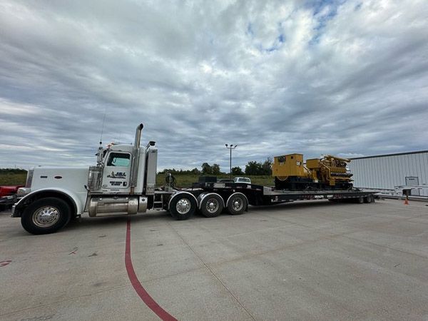 A semi truck is carrying a yellow tractor on a flatbed trailer.