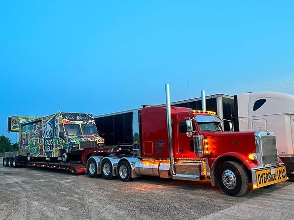 A red semi truck is carrying a trailer on a flatbed trailer.
