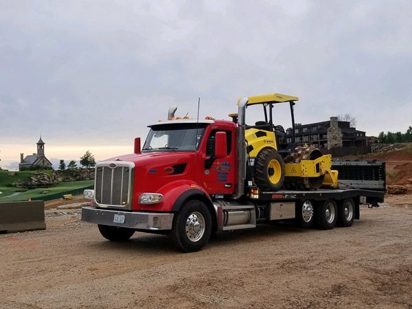 A red tow truck is carrying a yellow tractor on the back.