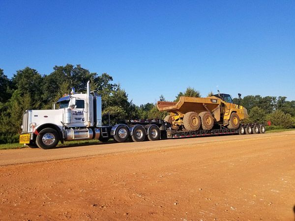 A semi truck is carrying a large bulldozer on a dirt road.