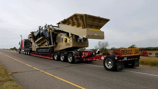 A semi truck is carrying a large machine down a highway.