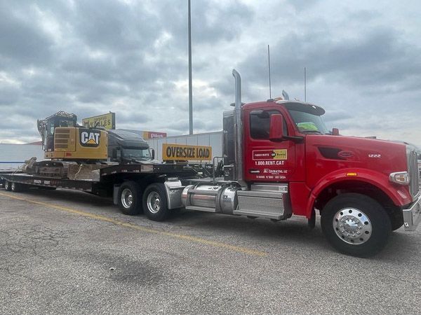 A red semi truck is carrying a cat excavator on a trailer.