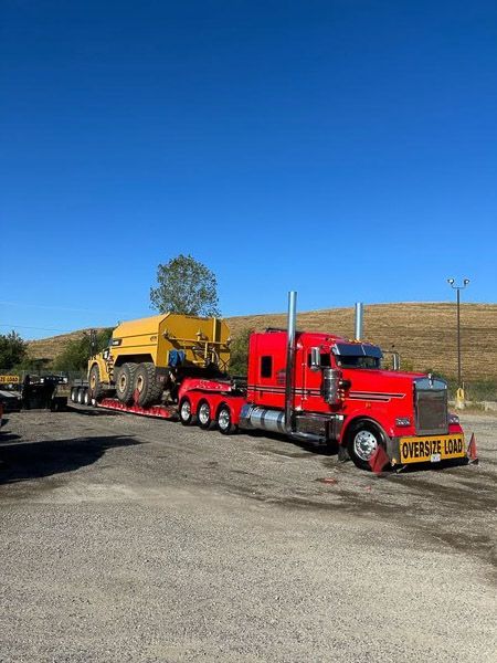 A red semi truck with a yellow trailer is parked in a parking lot.